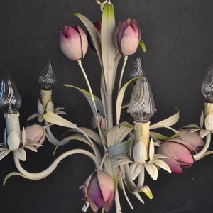 Pu&ograve; includere: Lampadario in metallo bianco con paralumi a forma di tulipano rosa e lampadine in vetro trasparente. Il lampadario ha un design floreale con foglie e steli.