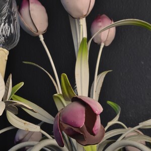Pu&ograve; includere: Un lampadario in metallo bianco con fiori a forma di tulipano rosa e viola. Il lampadario ha una base in corda bianca.