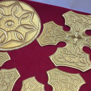 May include: A set of gold embroidered patches featuring a circular design and several cross shapes. The patches are on a red background.