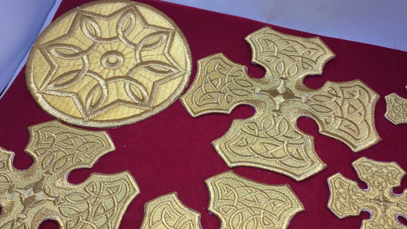 May include: A set of gold embroidered patches featuring a circular design and several cross shapes. The patches are on a red background.