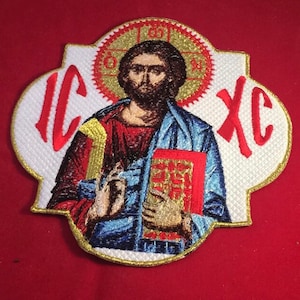 Peut inclure: Écusson brodé représentant une icône religieuse avec un halo, tenant un livre. L'écusson est de couleurs rouge, bleu, or et blanc. Les lettres "IC XC" sont en rouge sur l'écusson.