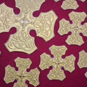 May include: A close-up of a red fabric surface with multiple gold embroidered crosses. The crosses have a Celtic knot design and are arranged in a random pattern.