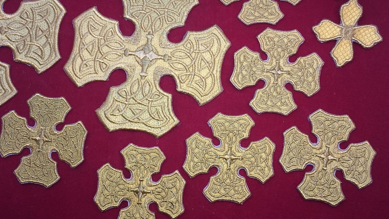 May include: A close-up of a red fabric surface with multiple gold embroidered crosses. The crosses have a Celtic knot design and are arranged in a random pattern.