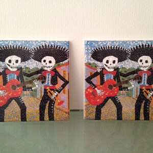 May include: Two skeleton figures in mariachi outfits playing musical instruments. The figure on the left is playing a red guitar and the figure on the right is playing a trumpet. The figures are standing on a colorful mosaic background.