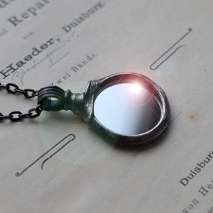 May include: A silver necklace with a round, mirrored pendant. The pendant has a textured, organic design and is attached to a black chain.