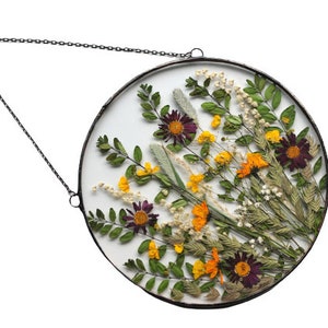 May include: A round glass frame with a metal chain for hanging, featuring a pressed flower arrangement with purple, yellow, and orange flowers and green leaves.