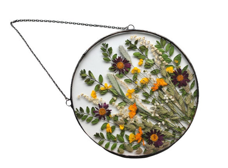 May include: A round glass frame with a metal chain for hanging, featuring a pressed flower arrangement with purple, yellow, and orange flowers and green leaves.
