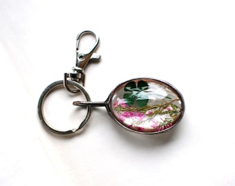 May include: A silver key chain with a clear oval charm containing a pressed four-leaf clover and pink flowers.