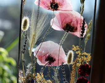 May include: A framed pressed flower art piece with pink poppies, lavender, and other dried flowers. The frame is made of metal and hangs from a chain.