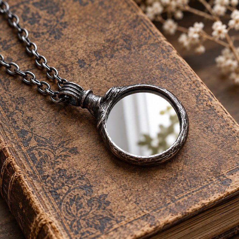 May include: A circular pendant necklace featuring a reflective mirror surface encased in a dark, weathered, textured metal frame with a matching link chain. The pendant has a rugged, aged appearance with visible grooves and a metallic finish.