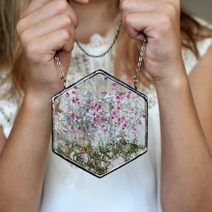 May include: A hexagonal glass pendant with a silver chain. The pendant contains pressed pink and white flowers and greenery.
