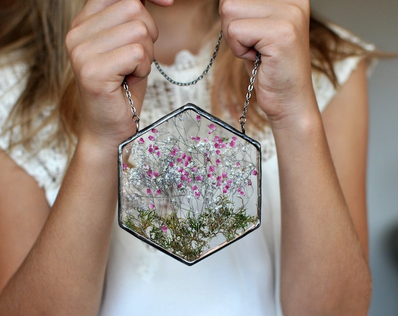 May include: A hexagonal glass pendant with a silver chain. The pendant contains pressed pink and white flowers and greenery.