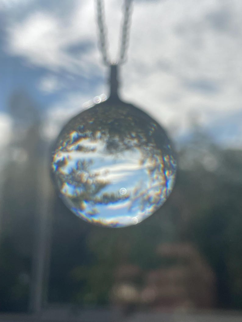 K&ouml;nnte beinhalten: Eine Halskette mit einem Anh&auml;nger aus klarem Glas in Kugelform und einer silbernen Kette. Die Kugel reflektiert den Himmel und die Wolken und erzeugt einen vertr&auml;umten und &auml;therischen Effekt.