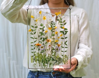 May include: A framed pressed flower art piece with a variety of yellow, orange, and purple flowers, and green leaves. The frame is made of metal and has a rustic look.