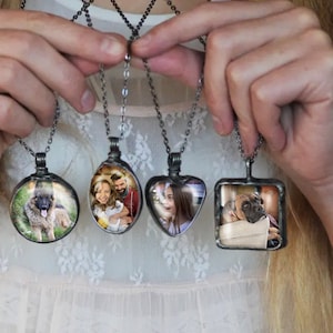 May include: Four silver necklaces with glass pendants featuring different photos. The pendants are round, oval, heart-shaped, and square. The photos include a dog, a family, a girl, and a dog.