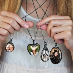 May include: Five silver necklaces with different shaped pendants. Each pendant has a photo inside. One pendant is a heart shape, one is a circle, and three are oval shapes.