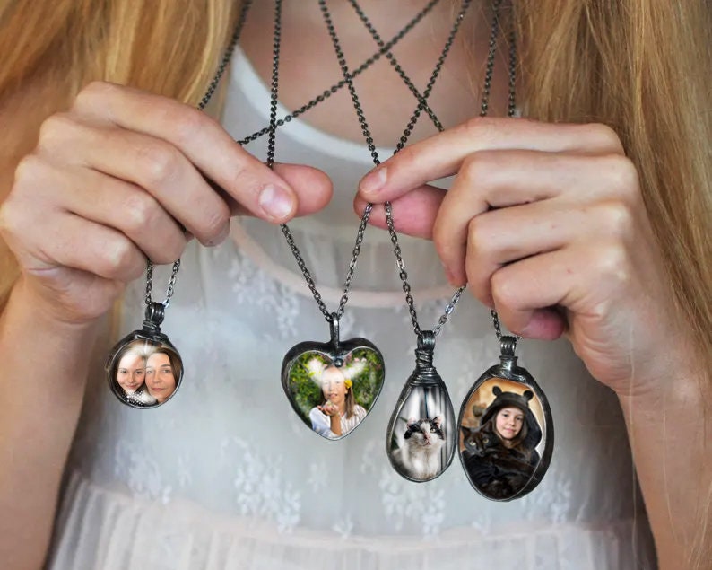 May include: Five silver necklaces with different shaped pendants. Each pendant has a photo inside. One pendant is a heart shape, one is a circle, and three are oval shapes.