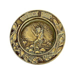 May include: A round brass trinket dish with a raised design of a pixie standing on mushrooms. The dish is inscribed with the words "Dartmoor Pixie".