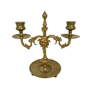 May include: A gold-toned brass candelabra with two candle holders and a decorative base featuring a grotesque face.