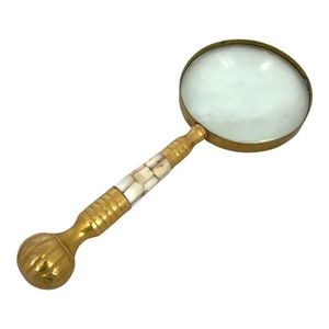 May include: A vintage magnifying glass with a brass frame and handle. The handle features a decorative design with alternating sections of brass and inlaid white material. The magnifying glass has a round lens.