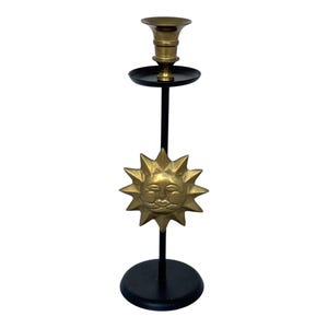 Peut inclure: Un bougeoir d&eacute;coratif en laiton avec un motif de visage de soleil. Le bougeoir a une base et une tige noires, avec un soleil en laiton au centre. Le haut contient un porte-bougie.
