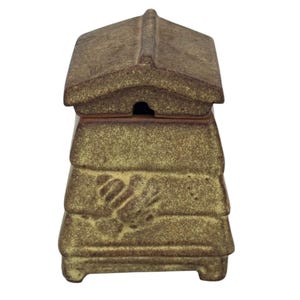 May include: A brown ceramic honey pot shaped like a traditional beehive with a removable gabled lid. The exterior features a speckled, textured finish and a moulded bee relief on the front. The container has a tiered, tapered body design.