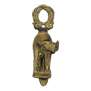 May include: A vintage brass cat-shaped door knocker. The knocker features a detailed design of a standing cat with a decorative loop at the top and a small, pointed base. The brass has a warm, aged patina.