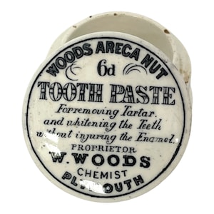 May include: Vintage white ceramic tooth paste container with a lid. The lid has black text: "WOODS ARECA NUT TOOTH PASTE" and "For removing Tartar and whitening the Teeth without injuring the Enamel."