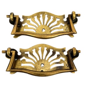 May include: A pair of antique brass drawer pulls with a sunburst design. The pulls are ornate and have a vintage look.