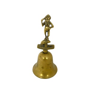 May include: A vintage brass bell with a small figure on top. The figure is a whimsical character with a hat and is standing on a platform that reads "CORNISH PITTIE". The bell has a classic shape and a warm, aged patina.