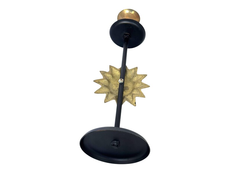 Peut inclure: Un bougeoir en m&eacute;tal noir avec un motif de soleil dor&eacute;. Le bougeoir a une base ronde et un petit sommet rond pour tenir une bougie. Le soleil est centr&eacute; sur la tige.