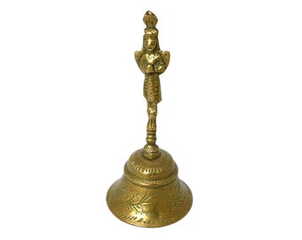 May include: A gold-colored bell with an ornate design. The bell has a handle with a small figure on top.