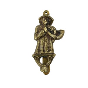 May include: Brass door knocker in the shape of a man playing a pipe. The knocker is inscribed with the words "R. Pon Horndicher".