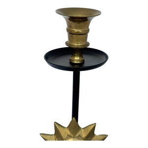 Peut inclure: Un bougeoir en laiton avec une tige noire et une base en forme d'&eacute;clat d'&eacute;toile. Le bougeoir a un dessus &eacute;vas&eacute; et un plateau circulaire. La base est dor&eacute;e et a un motif en forme d'&eacute;toile.