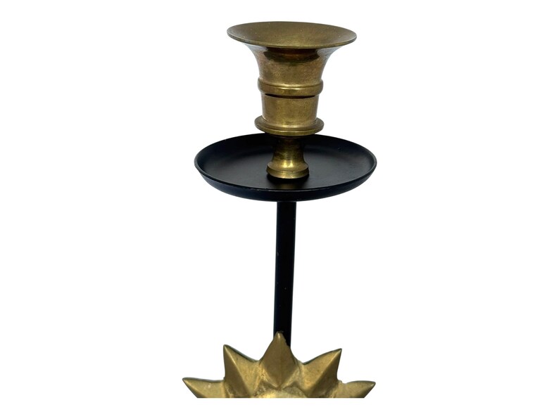 Peut inclure: Un bougeoir en laiton avec une tige noire et une base en forme d'&eacute;clat d'&eacute;toile. Le bougeoir a un dessus &eacute;vas&eacute; et un plateau circulaire. La base est dor&eacute;e et a un motif en forme d'&eacute;toile.