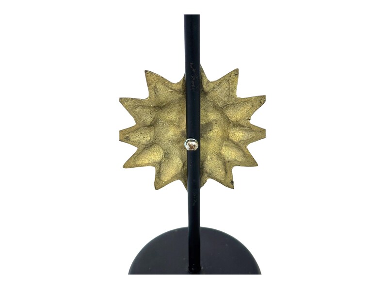 Peut inclure: Une sculpture d&eacute;corative en forme d'&eacute;clat de soleil avec un visage textur&eacute; de couleur or et des rayons pointus. L'&eacute;clat de soleil est mont&eacute; sur un support en m&eacute;tal noir avec une base circulaire.