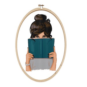 May include: A woman with brown hair is holding a teal blue book in front of her face. She is wearing a gray shirt.