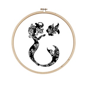 May include: Black and white embroidery hoop with a mermaid and a fish design. The mermaid is holding a fish in her hand. The design is intricate and detailed.