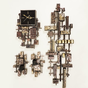 May include: A set of three wall sculptures made of metal with a geometric design. The sculptures are in shades of brown, gold, and black. The largest sculpture features a clock face with black hands and a black background.