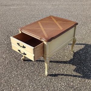 May include: A small, white end table with a drawer and a wood top. The top has a geometric pattern of inlaid wood.