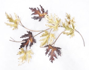 May include: A wall sculpture featuring a branch with multiple leaves in shades of brown and gold. The leaves are made of metal and have a textured surface.