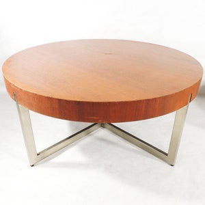 May include: A round wooden coffee table with a chrome metal base. The table top is a rich brown color and the base is a shiny silver.