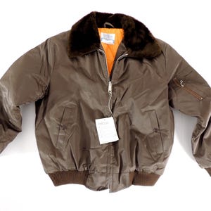 May include: A brown bomber jacket with a faux fur collar and an orange interior. The jacket has a zipper closure, two front pockets, and ribbed cuffs and hem. A tag is attached to the zipper.