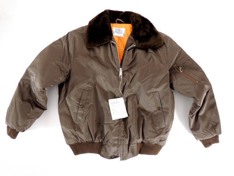 May include: A brown bomber jacket with a faux fur collar and an orange interior. The jacket has a zipper closure, two front pockets, and ribbed cuffs and hem. A tag is attached to the zipper.