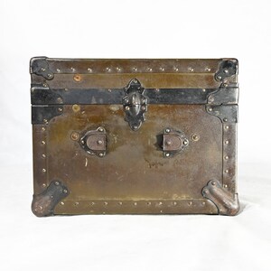 May include: A vintage green metal trunk with black metal accents and brass hardware. The trunk has a hinged lid and two clasps.