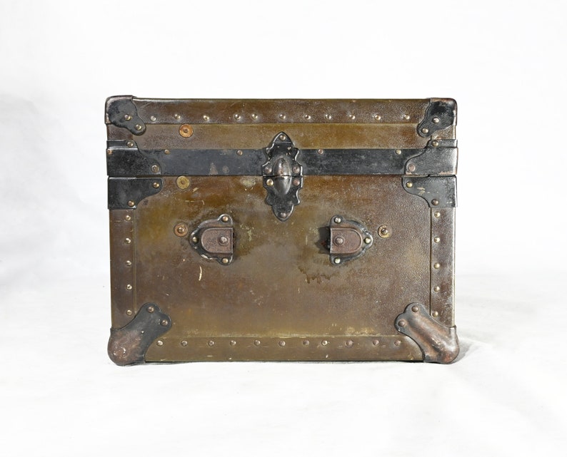 May include: A vintage green metal trunk with black metal accents and brass hardware. The trunk has a hinged lid and two clasps.