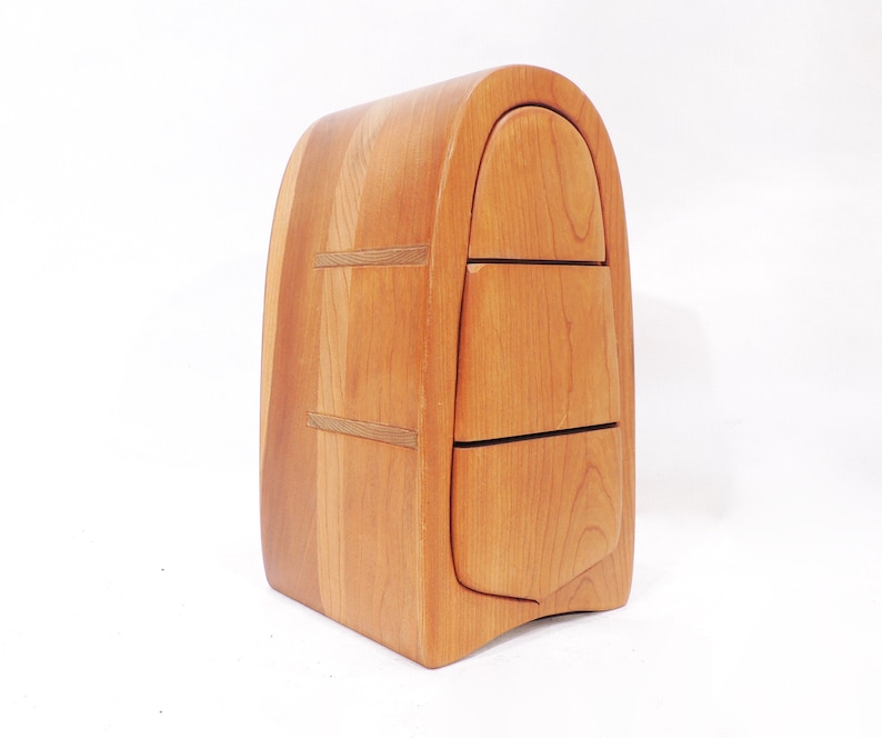 Pu&ograve; includere: Uno scrigno in legno con tre cassetti, ognuno con un fronte curvo. Lo scrigno &egrave; fatto di legno marrone chiaro e ha una parte superiore arrotondata.
