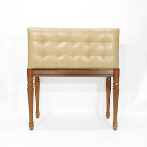 May include: A vintage-style bench with a rectangular, tufted, light tan leather seat. The seat rests on a dark brown wooden frame with four turned legs. The bench is set against a white background.
