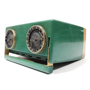 Puede incluir: Una radio vintage verde y dorada con dos diales redondos. Los diales tienen números negros y un centro negro con un anillo dorado.
