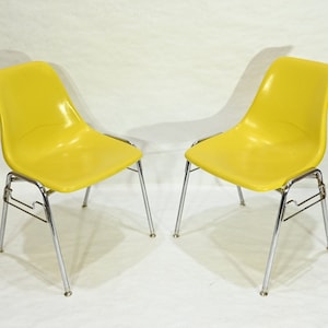 May include: Two yellow plastic chairs with chrome legs. The chairs are in a modern style and have a simple design.